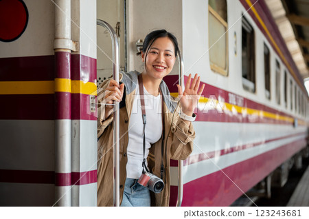 Smiling asian woman with camera is waving hand while coming down from carriage at train station 123243681