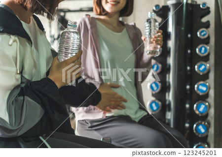 A woman talking to a pregnant woman who is exercising, stretching, and doing maternity training at the gym during pregnancy A woman talking to a pregnant woman who is exercising, stretching, and doing maternity training at the gym during pregnancy 123245201