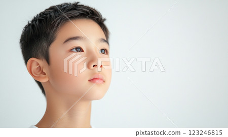 A young person with short dark hair gazes thoughtfully upwards, set against a bright white backdrop that emphasizes a serene mood. 123246815