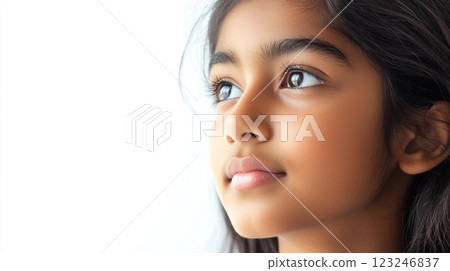 Young girl gazing upwards with serene expression, her dark hair framing her face against a bright, neutral backdrop, youthful reflection. 123246837