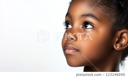 Young girl with a smooth complexion gazes upwards with striking eyes. She has an earring and is set against a solid white backdrop. 123246840