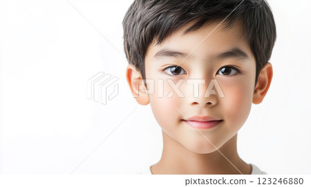 A portrait of a young boy with dark hair and brown eyes, smiling slightly against a bright, solid white background in a studio setting. 123246880