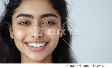 Close-up of a young woman's beaming face with perfect teeth and stunning eyebrows, set against a clean, soft-toned background. 123246929