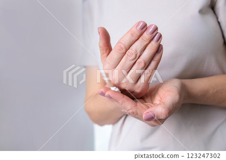 A mature woman of the pensioner age with dry skin smears moisturizing cream on her hands. 123247302
