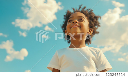 Child's Upward Gaze: A young boy with an afro gazes hopefully at the blue sky with clouds, radiating positivity and innocence. 123247314