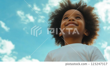 Young child looks hopefully up towards a bright blue sky filled with fluffy white clouds, full of optimism and wonder. 123247317