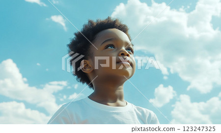 Young boy with a hopeful gaze towards a bright blue sky filled with puffy white clouds, embodying hope and aspiration for the future. 123247325