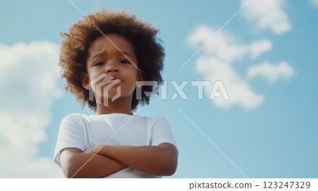 A young child poses with arms crossed against a bright blue sky. The confident look on their face gives an air of determination and self-assurance. 123247329