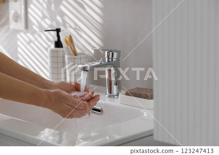 Female hands close up near white clean washbasin with running clean water. 123247413