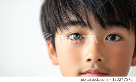 Close-up of a young boy's face. The child has black hair and brown eyes. He looks directly at the camera. Background is plain and white. 123247573