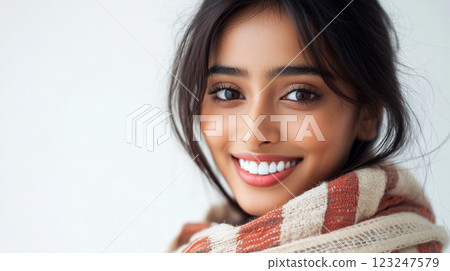 Close-up of a warmly wrapped woman with a gentle smile, showcasing a picture-perfect complexion and radiant appearance against a plain backdrop. 123247579