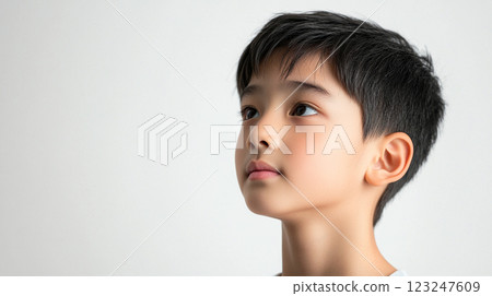 Young Asian boy looking upwards with a serious expression, capturing a moment of contemplation against a bright, neutral background. 123247609