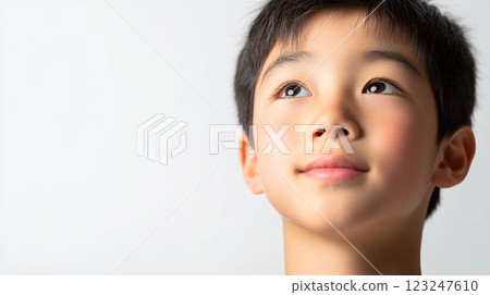 A young boy gazes upwards with a thoughtful expression, set against a clean, white background. Innocence and curiosity are evident in his eyes. 123247610