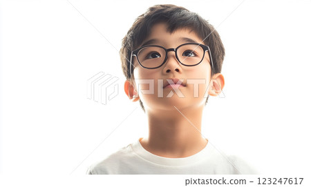 Young boy with black hair and glasses looking up on white background, representing curiosity and imagination in an isolated and focused manner 123247617