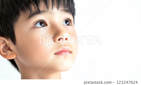 A young boy gazes upwards with curiosity and wonder, his eyes bright. The crisp background accentuates his features. 123247624