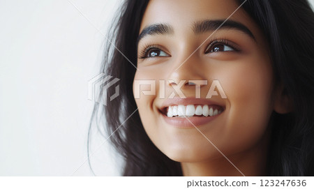 Radiant smile of a beautiful young woman looking upwards, her healthy teeth and glowing skin exuding confidence and natural beauty. 123247636