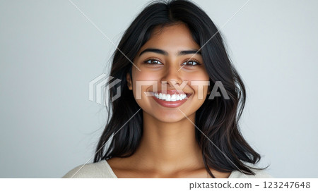 Radiant Portrait: A young woman with a bright smile and long dark hair poses against a neutral background, exuding confidence and warmth. Radiant Portrait: A young woman with a bright smile and long dark hair poses against a neutral background, exuding confidence and warmth. 123247648