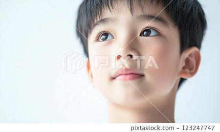 Pensive young boy gazes upwards with hopeful expression, dark hair framing his face against a softly blurred, light background. Innocence. Pensive young boy gazes upwards with hopeful expression, dark hair framing his face against a softly blurred, light background. Innocence. 123247747
