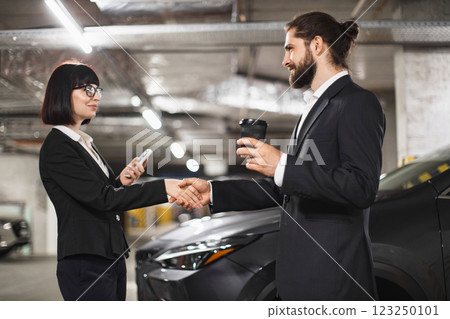 Caucasian businessman and businesswoman in formal attire shaking hands in underground car park, symbolizing business agreement or partnership. Caucasian businessman and businesswoman in formal attire shaking hands in underground car park, symbolizing business agreement or partnership. 123250101