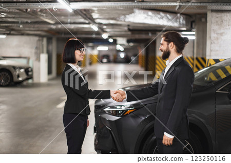 Caucasian businessman and businesswoman shaking hands in underground car park, symbolizing agreement and cooperation. Both in formal attire, engaging in business transaction. Caucasian businessman and businesswoman shaking hands in underground car park, symbolizing agreement and cooperation. Both in formal attire, engaging in business transaction. 123250116