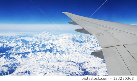 Aerial view from porthole of aircraft to beautiful Caucasus Mountains covered with snow. Traveling and tourism concept. Looking Out Window of a Plane. Scenic view with wing of an airplane to mountain 123250368