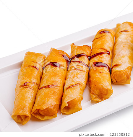 Crispy rolled snacks with sweet sauce on a white platter Crispy rolled snacks with sweet sauce on a white platter 123250812