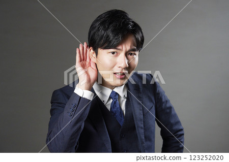 Businessman holding his hand to his ear, black background 123252020
