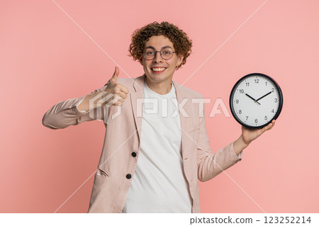 Excited Caucasian man showing time hour on wall office clock ok thumb up approve hurry up deadline Excited Caucasian man showing time hour on wall office clock ok thumb up approve hurry up deadline 123252214