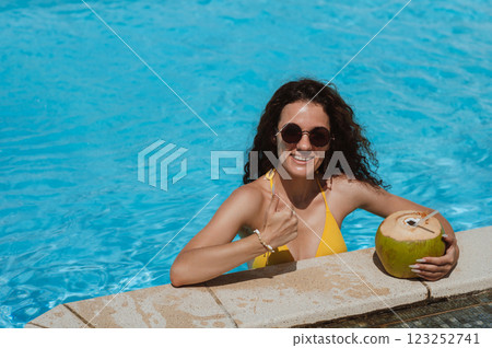 happy beautiful young woman in sunglasses with a drinking coconut is relaxing in swimming pool at hotel in resort in summer on vacation 123252741