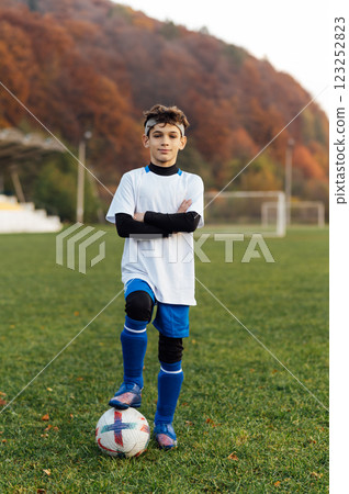 Young football player in white uniform posing on football field. School sports club. Young football player in white uniform posing on football field. School sports club. 123252823