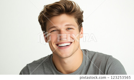 Young man with bright smile, styled hair, and grey t-shirt. Isolated on clean white background with soft, natural lighting. 123253565