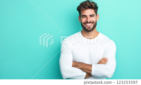Smiling man in white long sleeve shirt poses confidently against a bright turquoise background with arms crossed and a warm, inviting smile. 123253597