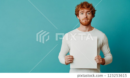 Red-haired man presents blank white card against a teal background, offering a space for personalized messages or information. 123253615