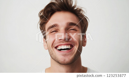 A young man with tousled brown hair and a neatly trimmed beard flashes a wide, genuine smile against a bright white background. Happiness radiates! 123253877
