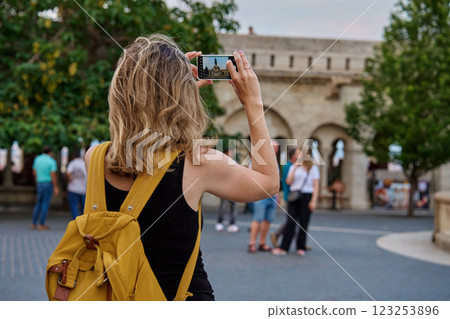 Female tourist with yellow backpack taking photo of historic landmark in Budapest during travel. Woman using smartphone to capture travel and sightseen moments in European city Female tourist with yellow backpack taking photo of historic landmark in Budapest during travel. Woman using smartphone to capture travel and sightseen moments in European city 123253896