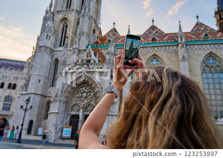Female tourist capturing photo of historic cathedral in Budapest using smartphone. Traveler walking at city street 123253897