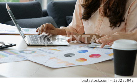 Asian Female freelance using laptop at home office desk. Woman reading financial graph chart Planning analyzing marketing data. Asian female people working office firm with business stuff, coffee cup Asian Female freelance using laptop at home office desk. Woman reading financial graph chart Planning analyzing marketing data. Asian female people working office firm with business stuff, coffee cup 123253942