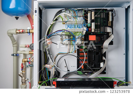 Close-up of boiler control panel with exposed electrical wiring, circuit board, and terminal connections. Modern heating system with complex electronic components 123253978