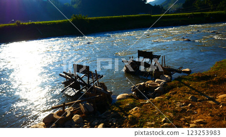 Wood water wheel Baler Machine in Agriculture Farm impeller lifted pumping water in river. Wooden Water Baler Machine green garden Farm blades by windy natural. Sustainable Resources Environment 123253983