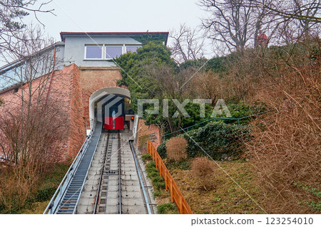 Schlossberg funicular in Graz, Austria. Red cable car ascending steep track through tunnel entrance surrounded by greenery 123254010
