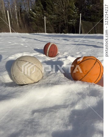 Three basketballs partially buried in fresh snow on an outdoor court. High quality photo 123254217