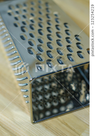 Stainless steel box-shaped four-sided kitchen grater lies wooden cutting board . High quality photo 123254219