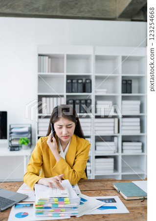 Focused businesswoman analyzing charts and data while on a phone call in a modern office setting 123254668