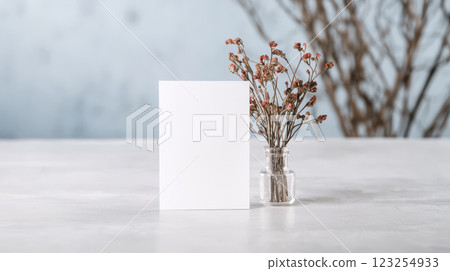 Blank card beside dried flowers in glass vase on table 123254933