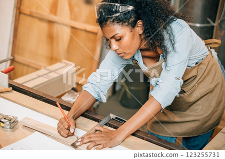 African American carpenter woman drawing a line on wood with a pencil and ruler in workshop. Focused on precise measurements, woodworking, and construction tasks in carpentry, National Carpenters Day African American carpenter woman drawing a line on wood with a pencil and ruler in workshop. Focused on precise measurements, woodworking, and construction tasks in carpentry, National Carpenters Day 123255731