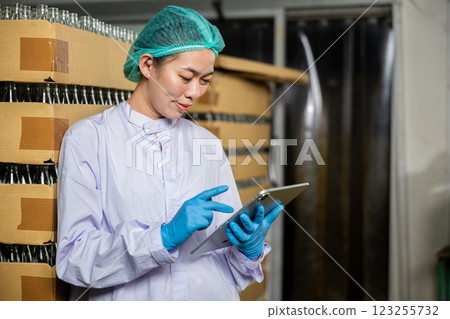 A dedicated QC woman at beverage factory uses a digital tablet to inspect items on the conveyor belt. Her role encompasses quality control while examining the bottling line for liquid manufacturing. A dedicated QC woman at beverage factory uses a digital tablet to inspect items on the conveyor belt. Her role encompasses quality control while examining the bottling line for liquid manufacturing. 123255732