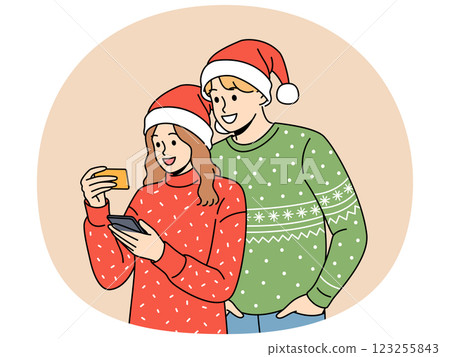 Couple in christmas clothes makes purchases on phone mobile app and uses credit card to pay 123255843