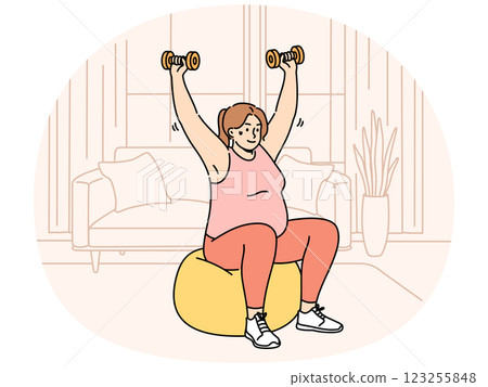 Woman doing sports, wanting to lose weight, lifts dumbbells sitting on inflatable fitness ball 123255848