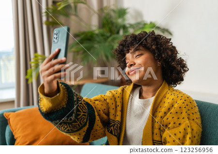 African American girl holding smartphone having video chat. Female blogger chatting with best friends in social network. Young woman having virtual meeting online chat video call at home African American girl holding smartphone having video chat. Female blogger chatting with best friends in social network. Young woman having virtual meeting online chat video call at home 123256956