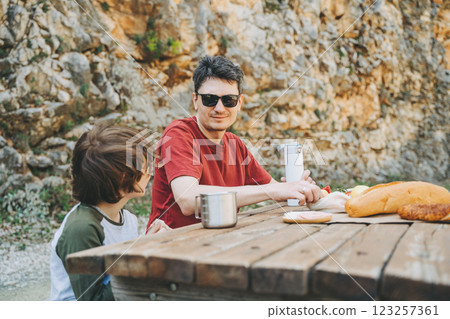 Close-up view of father and his school boy son on a family picnic in the mountains. Child kid and his dad taking a rest and enjoying a picnic while hiking in the mountains 123257361